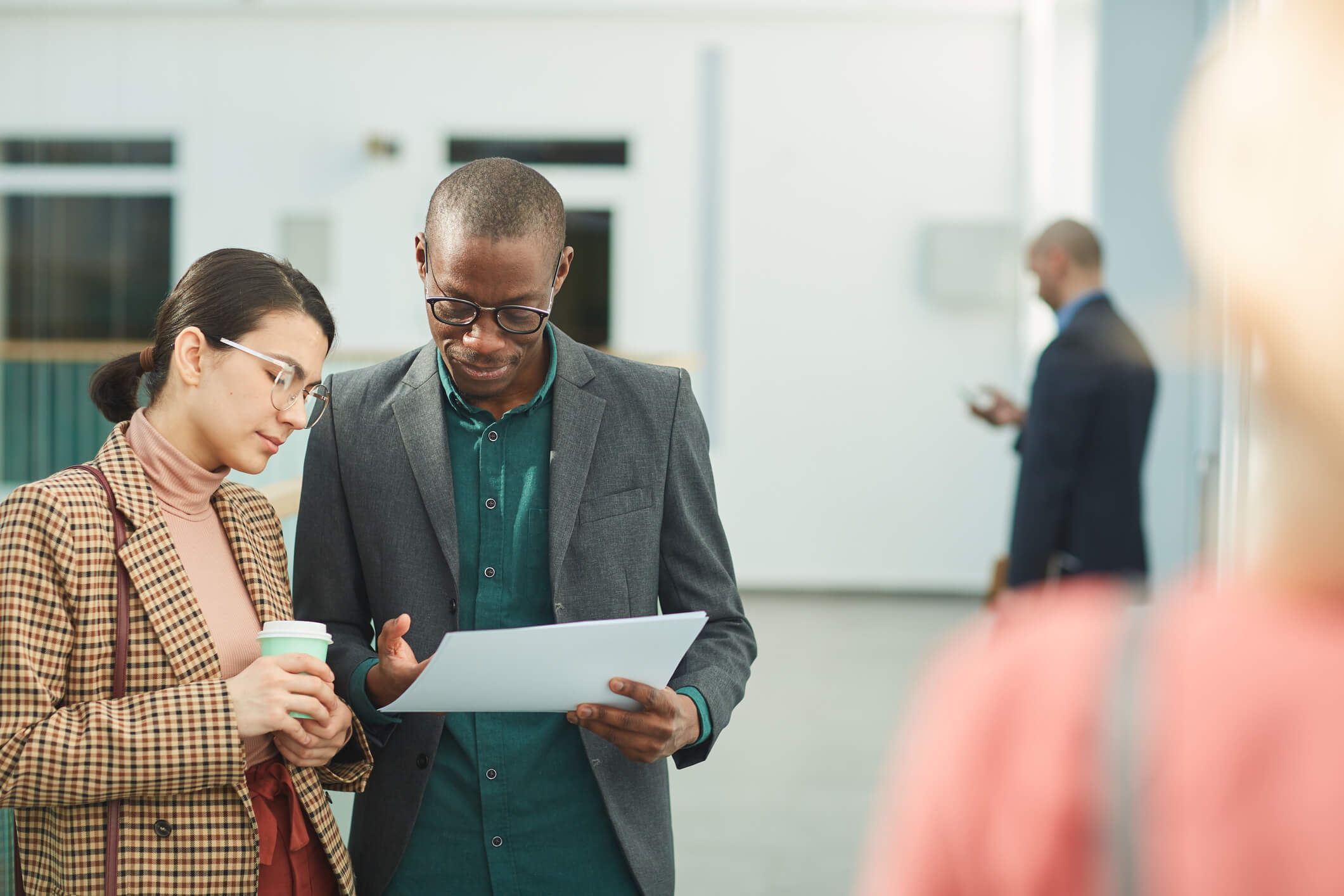 Two coworkers are standing up outside and looking at a document; they have serious expressions.